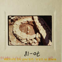 Image shows an ancient stone structure, possibly a well or pit, with stones around it, set against a natural backdrop.