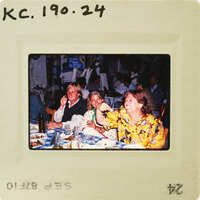 A vintage photo of three people sitting at a restaurant table, smiling and enjoying their time together. Catalog number KC.190.24