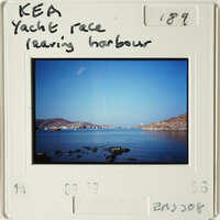 Landscape photograph showing calm waters with distant mountains and boats, viewed from a coastal perspective.