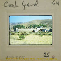 A vintage photograph of a rural landscape with mountains, trees, and a building.