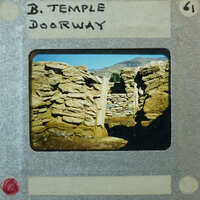 Detail of stone walls forming a doorway with mountains and sky in the background.