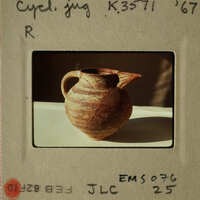 Ancient clay pot with two handles and a spout, sitting on a white surface.