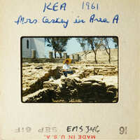 Woman sitting on ancient ruins with Mediterranean landscape in background.