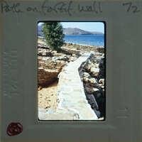 A vintage photo of a stone path leading to the sea with mountains in the background.