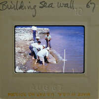 A group of men working on a sea wall near water.