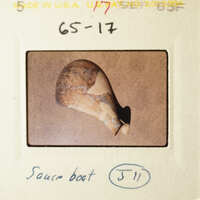 The image shows a broken pottery piece with visible cracks and missing parts, placed on a surface with a focus on its damage.