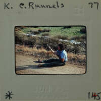 A man sitting on the ground holding wire from balloon.