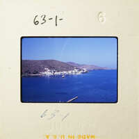 A photograph of a coastal scene with blue water, boats, and mountains under a clear sky.