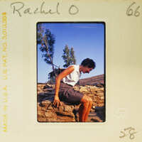 Woman sitting on a rock wall with trees in the background.