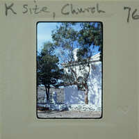 A photograph of a white church with trees and mountains in the background, placed on an old film negative holder.