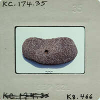 A small, round rock with a hole through it on a white surface.