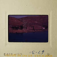 A scenic view of a body of water with a village and hills in the background, taken from an elevated perspective.