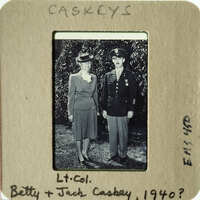 A man and woman, possibly a couple, dressed formally with military insignia on his uniform, standing together outdoors.
