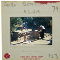 Slide with two men working on terracotta statue repair outdoors.