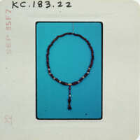 A bead necklace with a tassel, photographed against a blue background and placed on a white card.