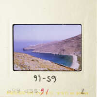 A photograph of an old slide featuring a scenic view of a coastal landscape with a clear sky, a large body of water, and a rocky shoreline.