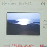 A photograph of a serene harbor with a mountainous coastline and sunset, displayed on an old film strip.