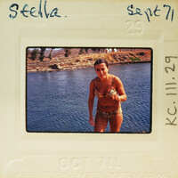Woman standing on the shore of a body of water, wearing a bikini and smiling. Catalog number KC.111.29
