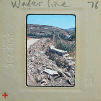 A photo of a dirt road with a water line and stone retaining wall.