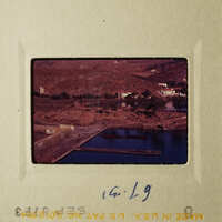 A vintage photo capturing a serene landscape with a body of water, buildings, and a clear sky.