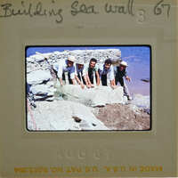 A group of men posing together on a rocky shoreline with the ocean in the background.