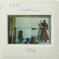 A clay figurine of a woman with a skirt, displayed on a wooden stand.