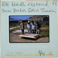 Four men standing around a large wooden structure with mountains in the background.