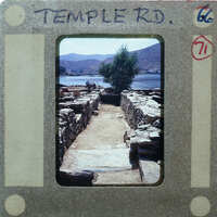 A photograph of a stone path leading to water, with mountains in the background.