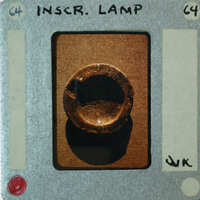 A small, round, metallic object with a hole through the center is displayed on a card.