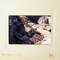 An archaeological site with stone ruins, featuring an excavation area and a person standing nearby.