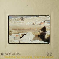 The photo shows a rocky beach scene with construction materials and equipment, possibly indicating ongoing work on the shoreline.