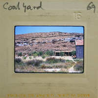 A photograph of a coal yard with mountains and buildings in the background.