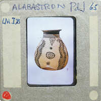An image of an alibastron vase with an intricate design, placed on a white surface.