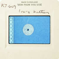 A circular object with intricate patterns, possibly an ivory button, on a blue background with measurements.