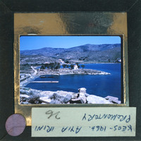 A vintage postcard with a photo of a coastal landscape, featuring a harbor and mountains, enclosed within a cardboard frame with handwritten text on the back.