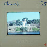 Photo of a church with a body of water and mountains in the background, displayed on an old film strip.