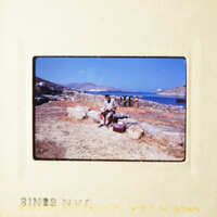 A man sitting on rocks next to the ocean, with mountains in the background.