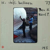 Two men working on a large, inflated balloon outdoors.