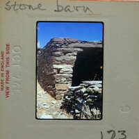 Old stone building on a hillside with grass and rocks around it.