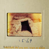This is an old photograph of an underground cave entrance with a stone archway, taken from above.