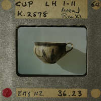 A small, dark-colored cup with a handle on a white surface.