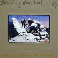 Men working on a stone wall by the water.