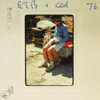 A vintage photo of a person sitting on a bench with a cat, taken outdoors.