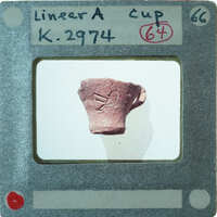 A photograph of a small, red clay pot with markings on it, K.2974.