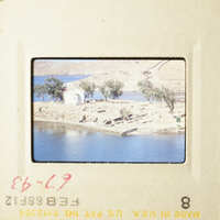 This is a photograph of a serene landscape featuring a body of water, a small building, and trees, with a boat visible on the water.