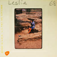 Woman sitting on stone ruins with a camera, taking a photo.