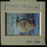 Ancient vase with visible cracks and peeling paint, sitting on stone floor.