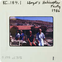 Old photo of four people sitting outside a house with mountains in the background.