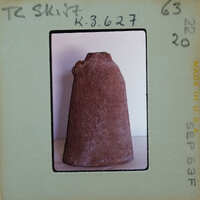 A photograph of a brown pottery item with a handle, displayed on a white surface.