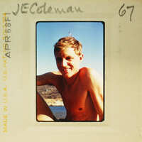 A man with short hair, smiling and shirtless, sitting on a boat.